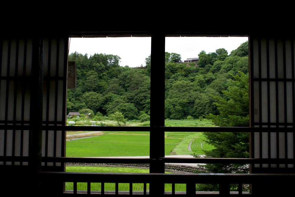 格子窓の向こうに広がる山あいの田んぼと森
