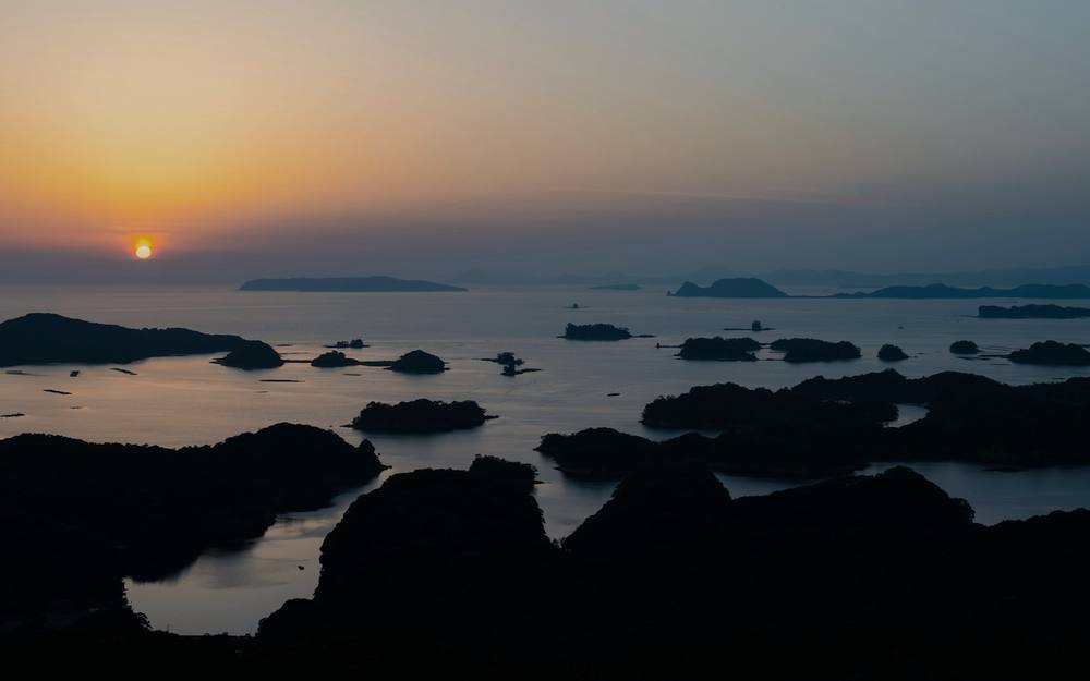 夕暮れの海に小さな島が連なり、水平線に日が沈んでいく