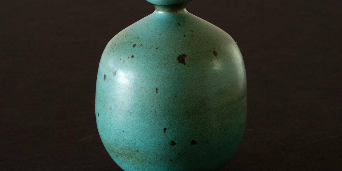 A small turquoise ceramic vase on a dark background