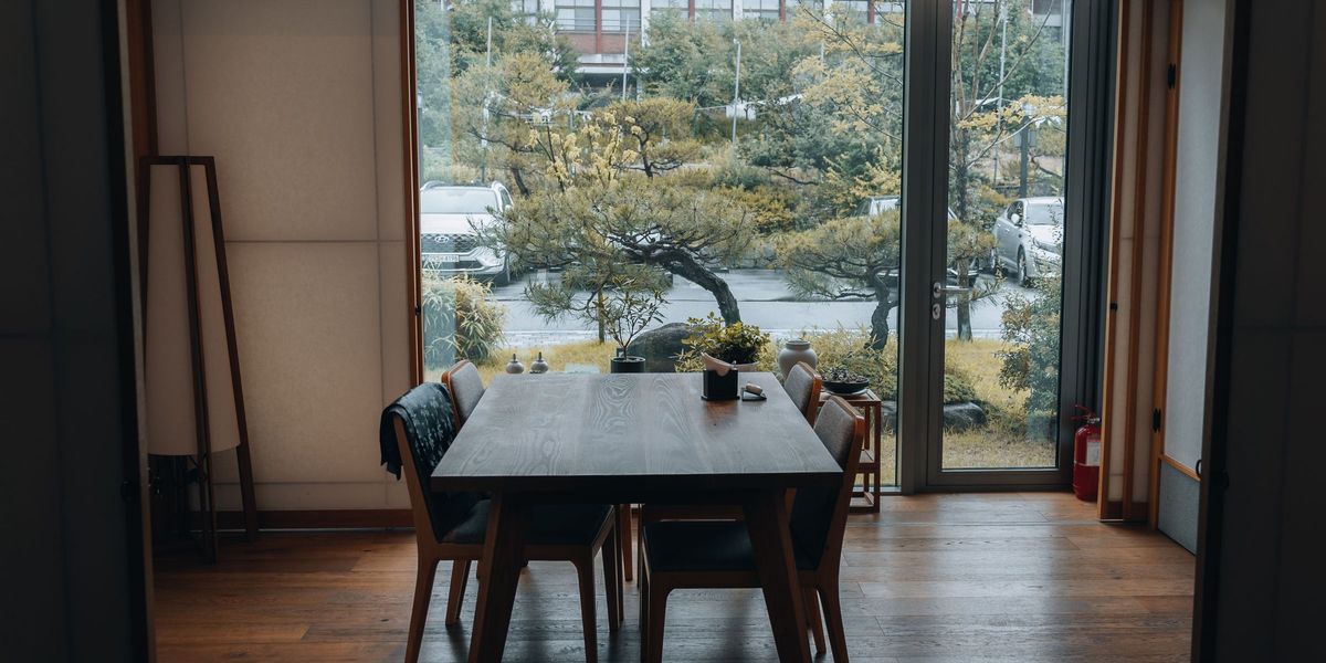 A round wooden table and a dark wooden chair against a pale wall