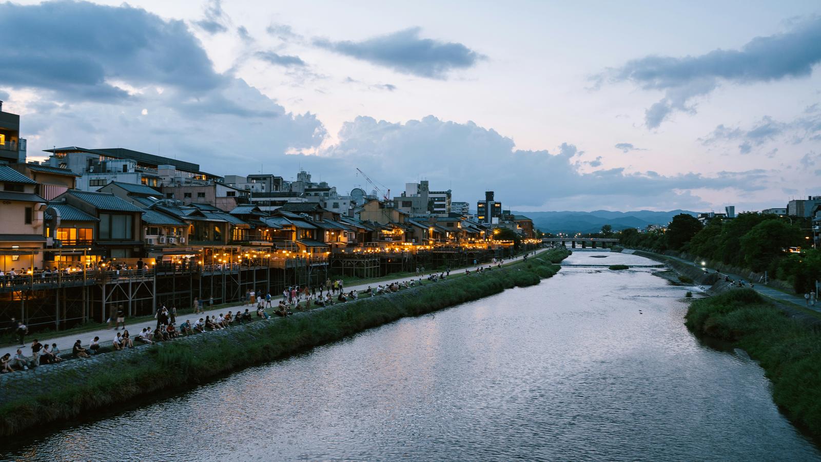 Riverside dining terraces lit up along the Kamo River in Kyoto at dusk, with hills in the distance