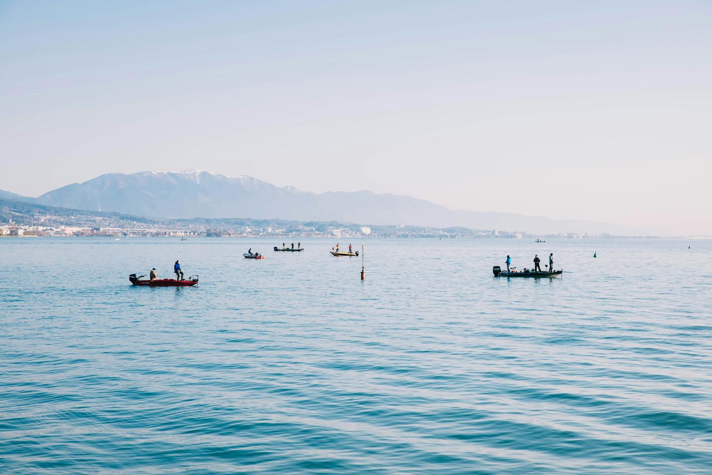Pequeñas barcas de pesca sobre el agua tranquila y pálida de un gran lago de Shiga, con una montaña en la otra orilla
