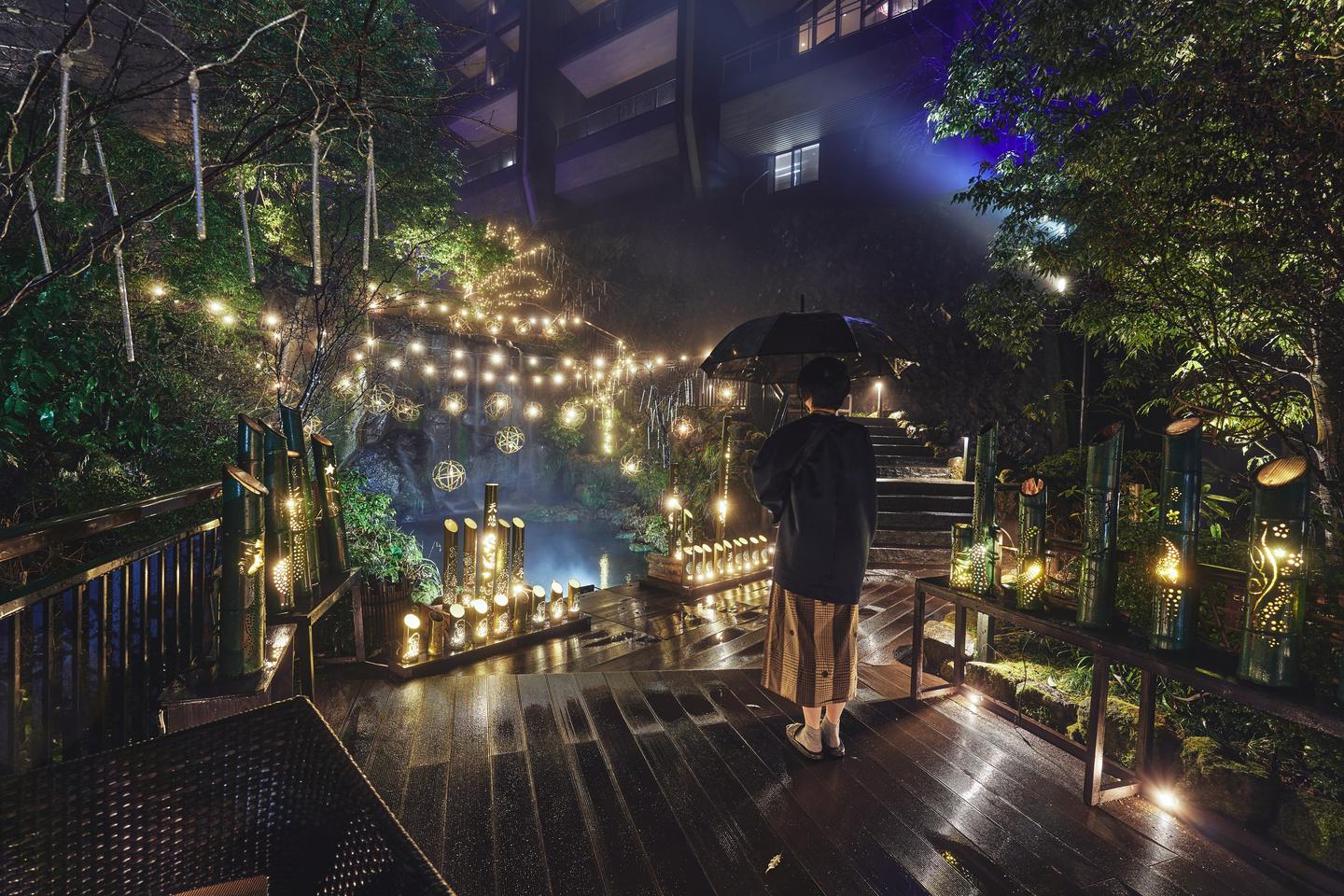 A person holding an umbrella on a wet wooden deck in a softly lit garden in Hakone at night