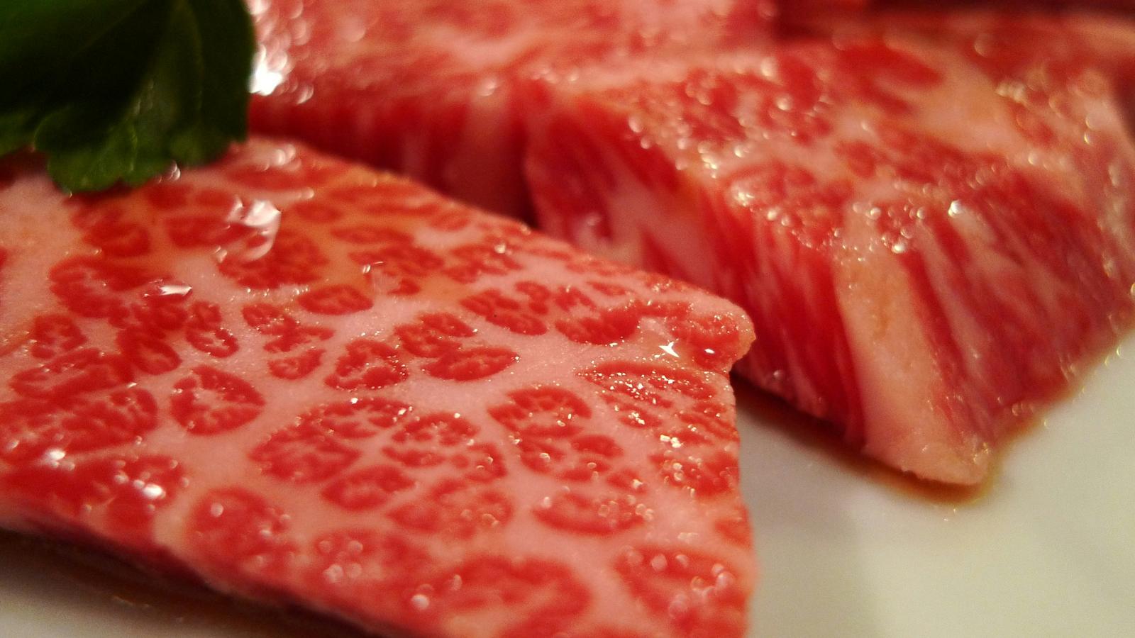 Thick slices of raw wagyu beef with fine marbling, set beside a green leaf