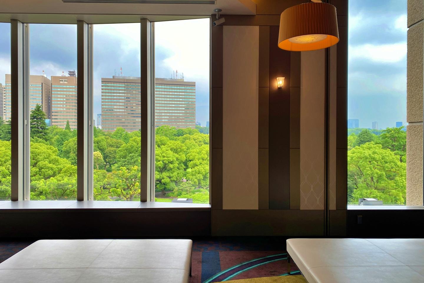 Cushioned benches in a quiet room with tall windows looking out over green treetops and office towers