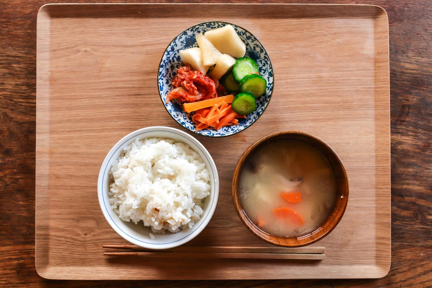 A simple meal on a wooden tray: a bowl of rice, miso soup with carrots, and a small plate of pickles