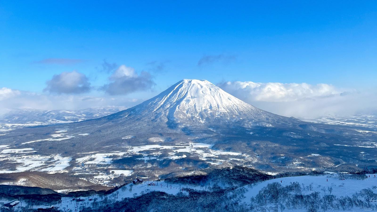 Snow-covered Mount Yotei under a blue sky, seen from Niseko above a snowy plain