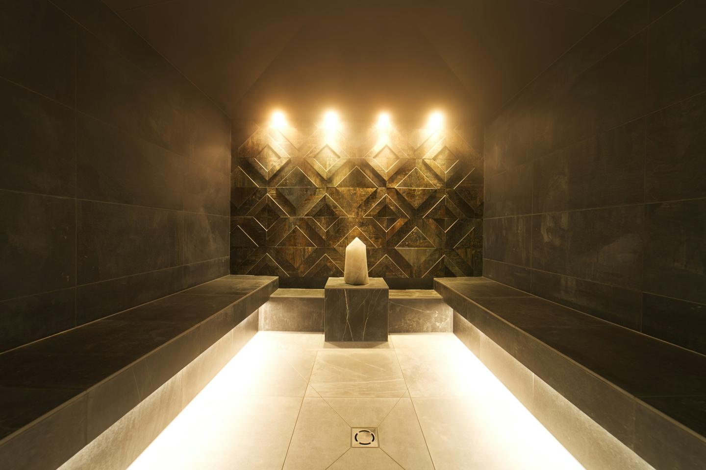 A steam room with stone benches, a single candle and warm lights in the wall