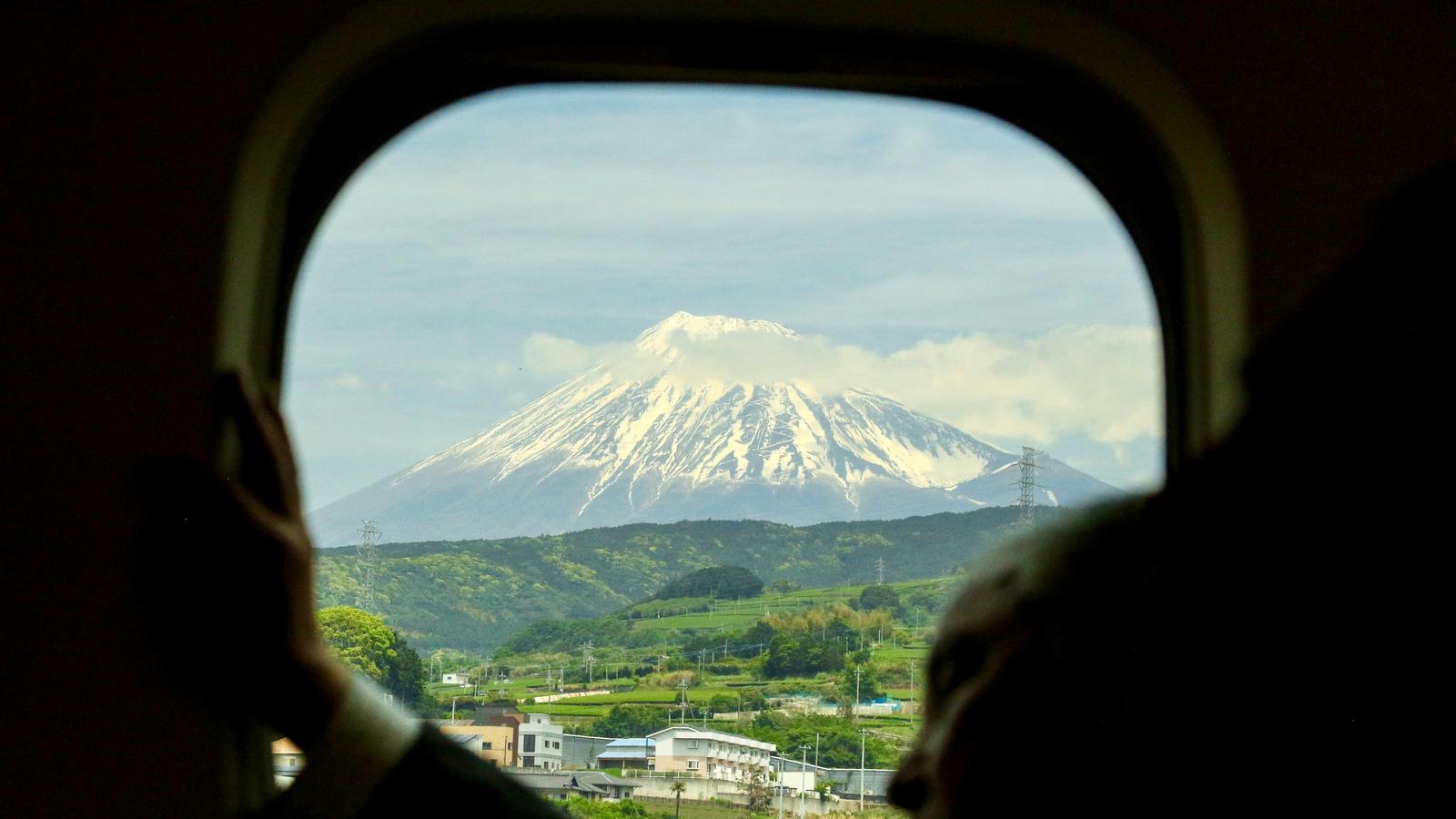 Mount Fuji seen through a window, with green hills and houses below