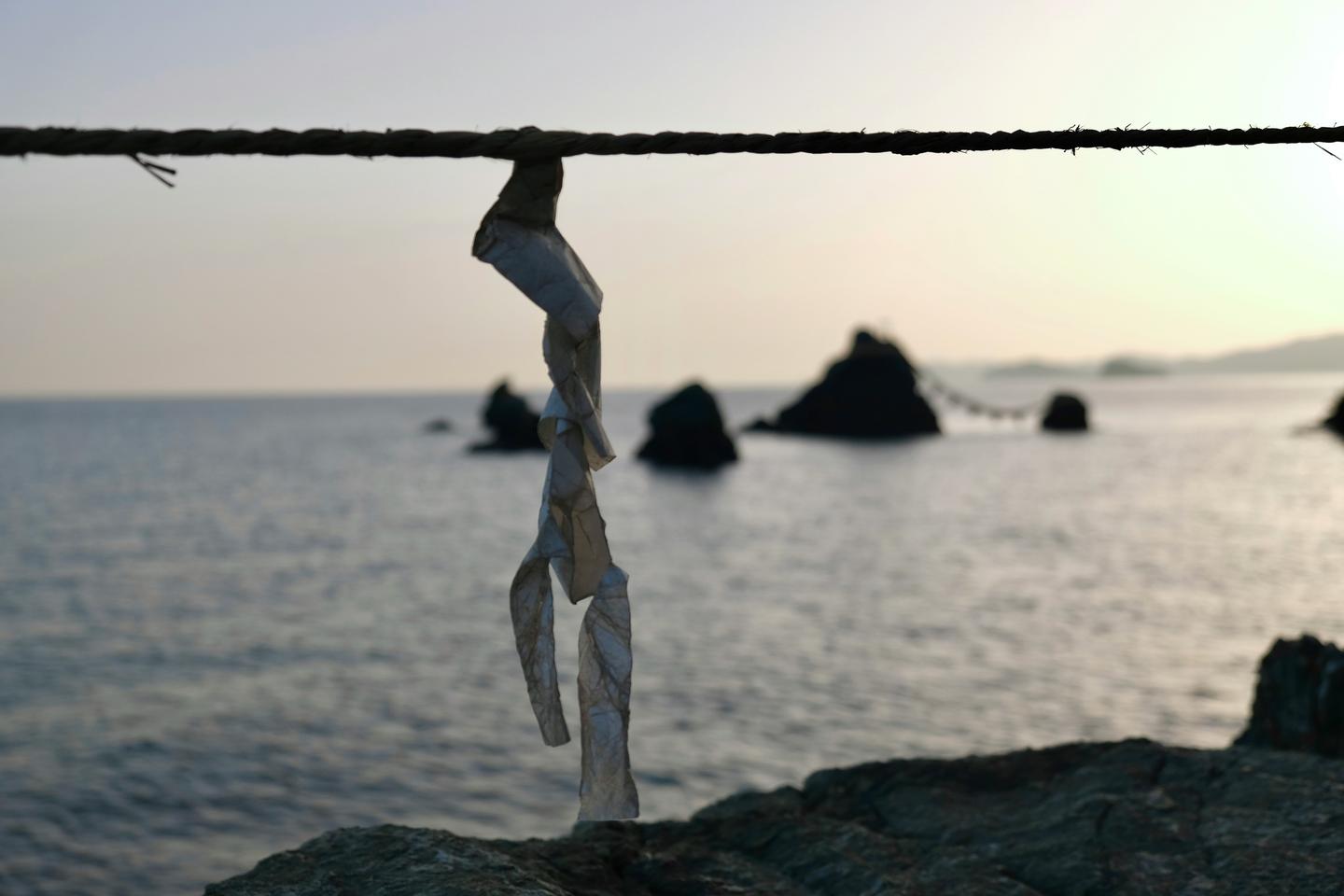 Une corde sacrée ornée d'un ruban de papier tendue au-dessus de la mer à Futami, avec les rochers Meoto Iwa au crépuscule.