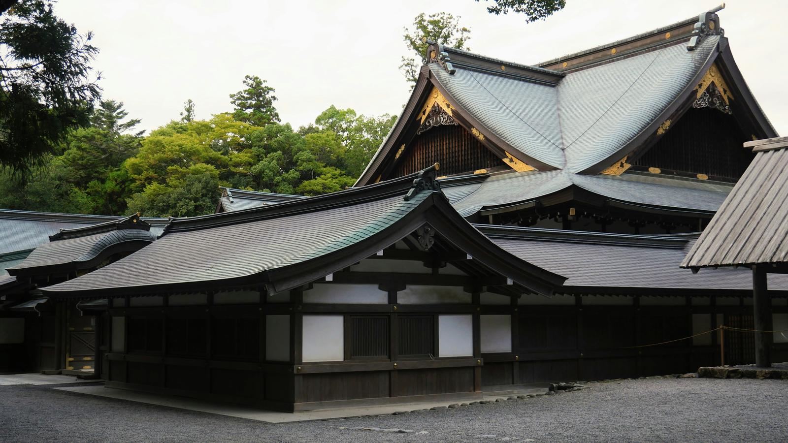 Des pavillons en bois aux toits de cuivre vert et ornements dorés se dressent sur le gravier d'Ise Jingu, entourés d'arbres.