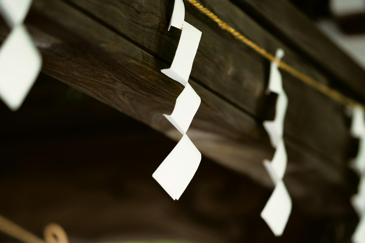 Zigzag white paper shide hanging from a straw rope under dark wooden eaves