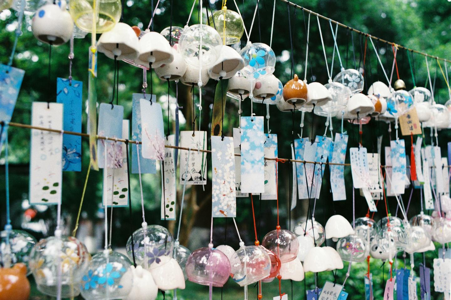 Rows of glass furin wind chimes with paper strips hanging outdoors under green leaves
