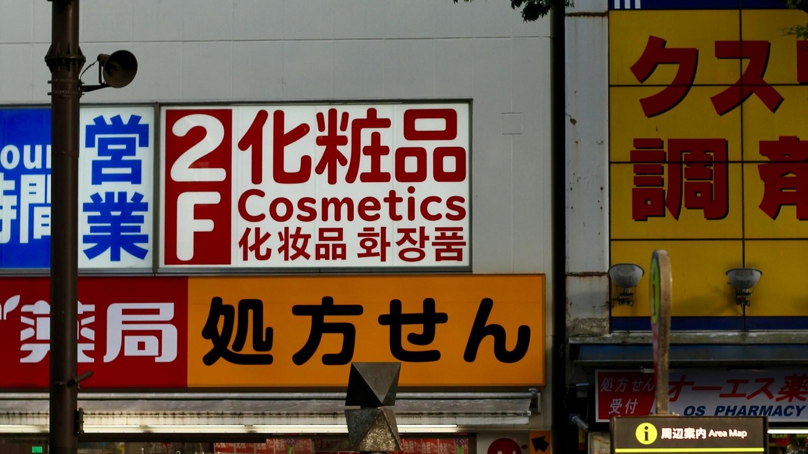 People walking past a building whose signs advertise cosmetics on the second floor and a pharmacy below