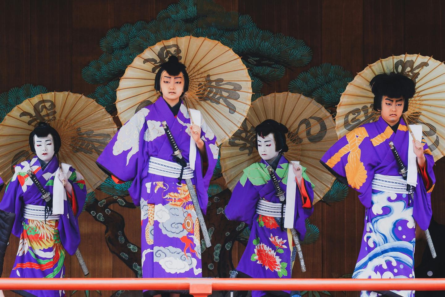Young performers in purple kimono holding paper umbrellas on an outdoor kabuki stage in Asakusa