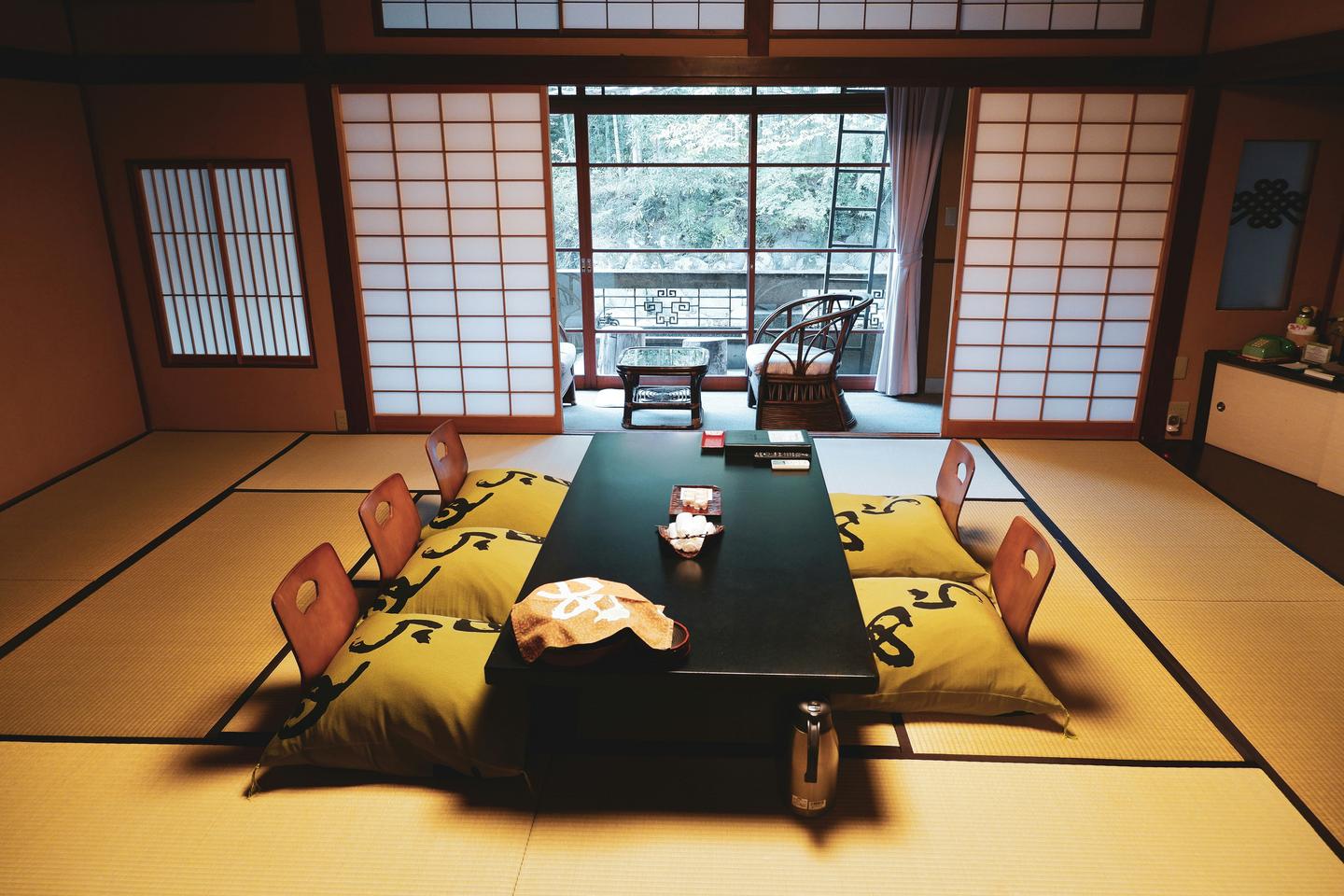 A tatami guest room at a ryokan with a low lacquered table and floor chairs set before a window onto the garden