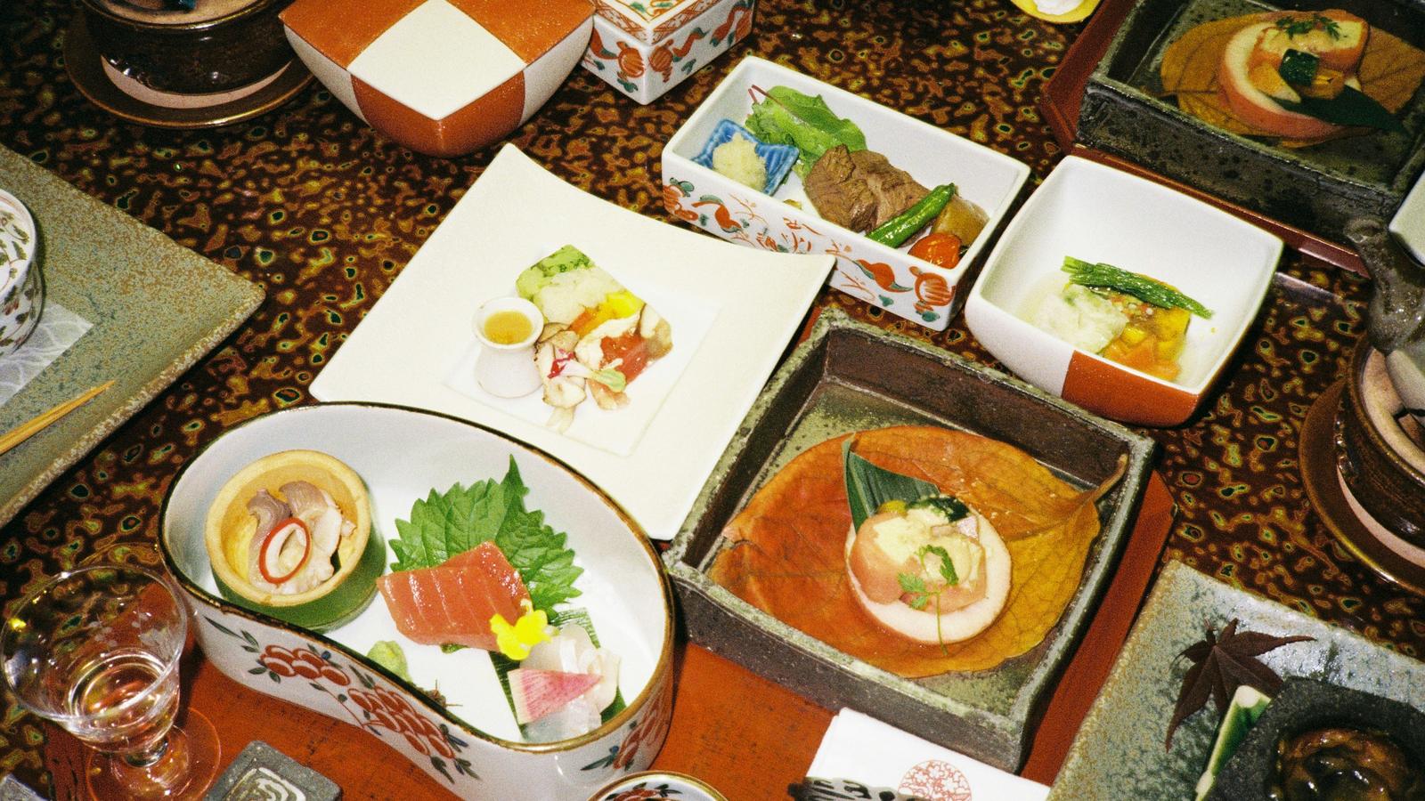 A kaiseki dinner laid out on a table: sashimi, small simmered dishes and lidded bowls in porcelain and lacquer