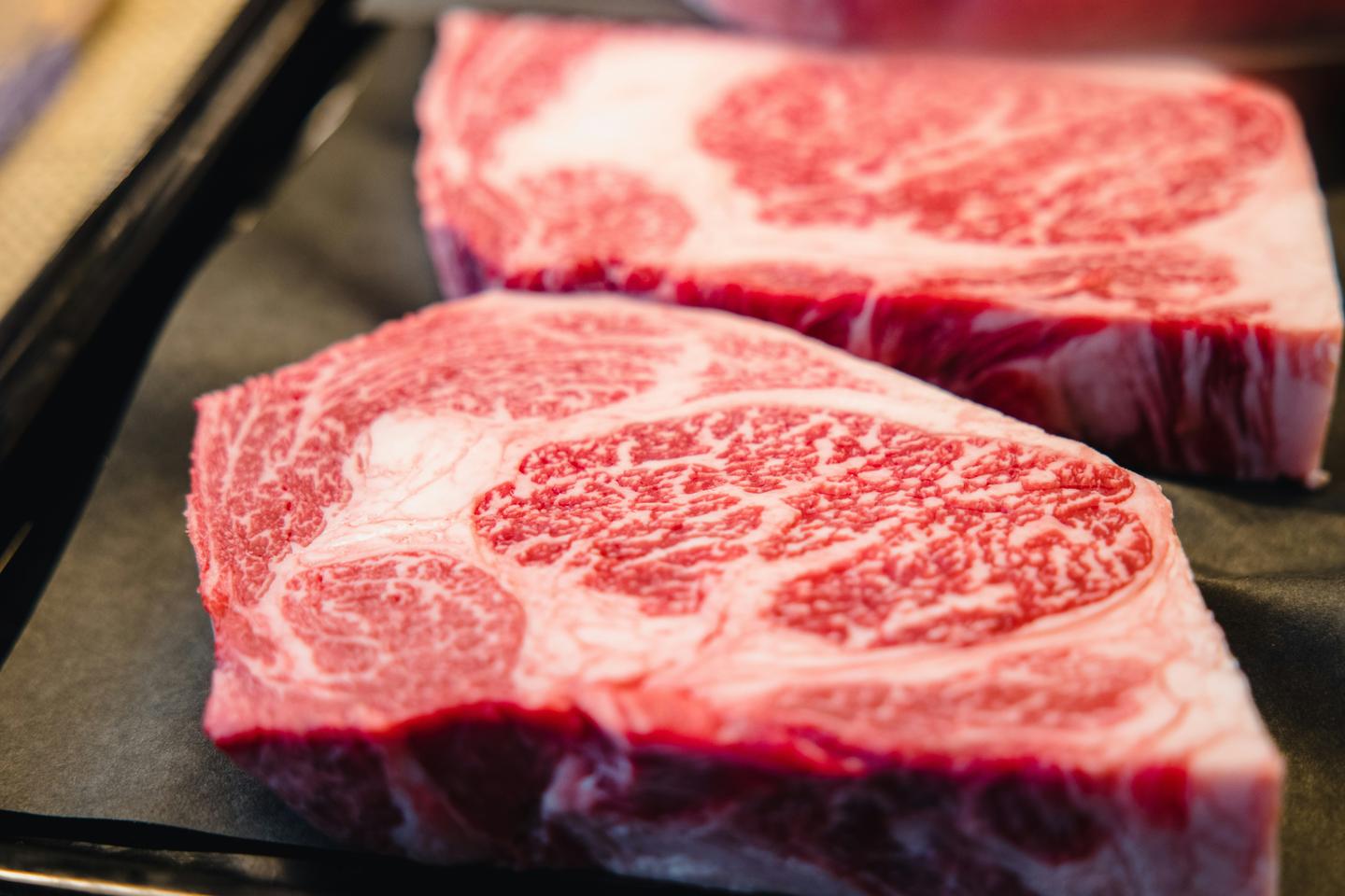 Two thick raw steaks of wagyu with dense white marbling on a dark plate