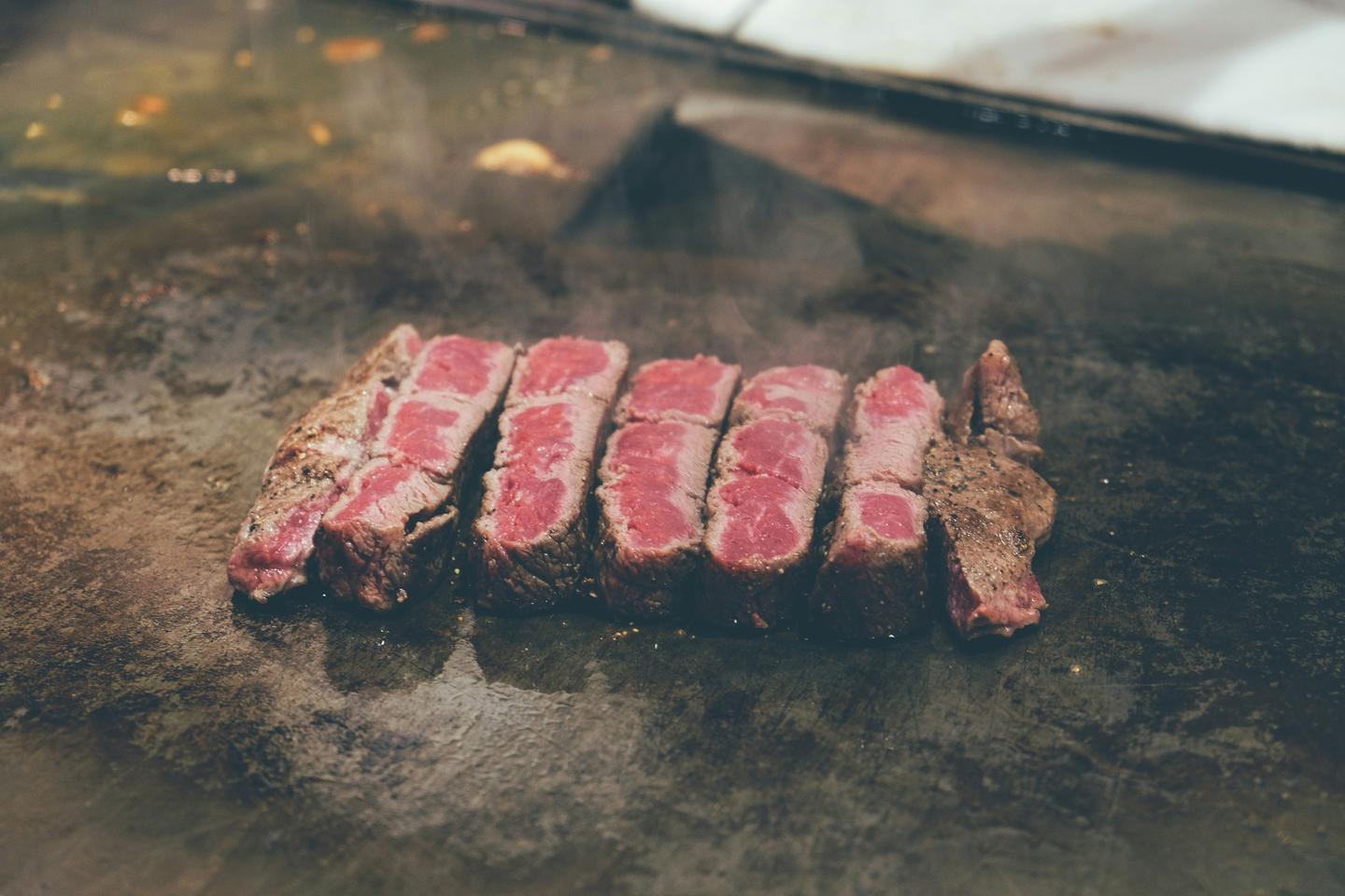 A seared beef steak cut into slices on a teppanyaki griddle, pink in the centre