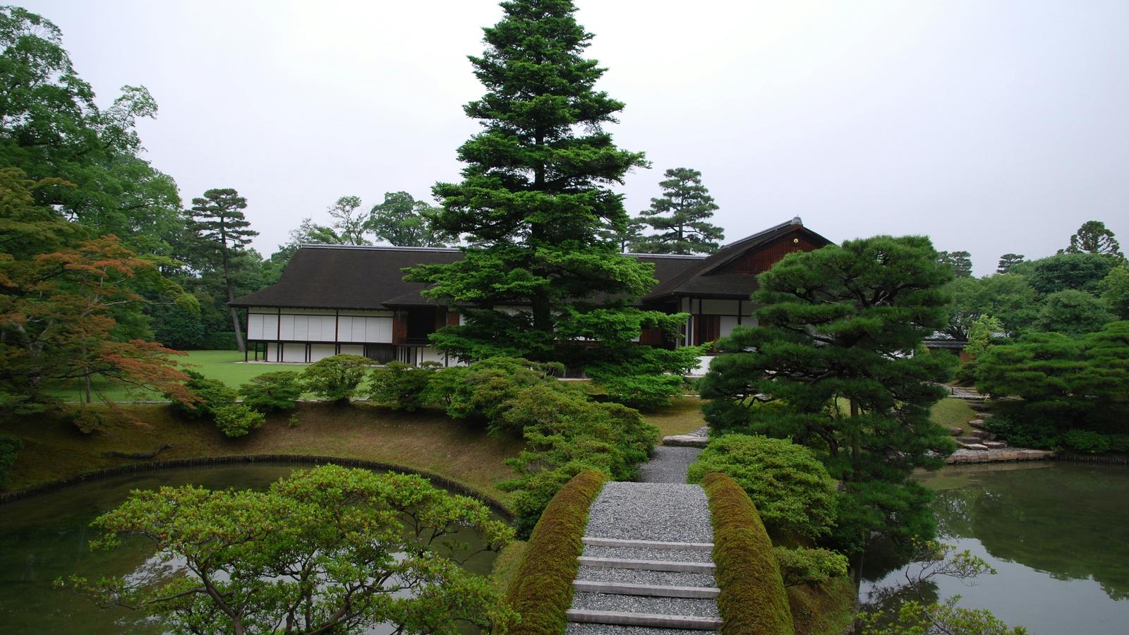 A stroll garden in Kyoto with a stone path leading between clipped shrubs to a pond and a low wooden villa