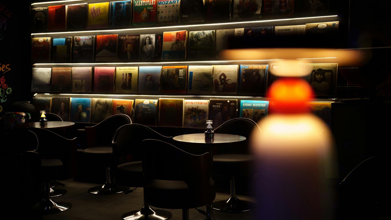 A dimly lit bar with an illuminated wall of vinyl records and seating