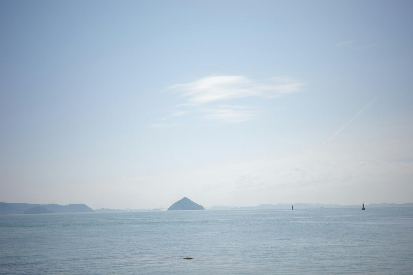 A calm, pale blue Seto Inland Sea with a small conical island on the horizon