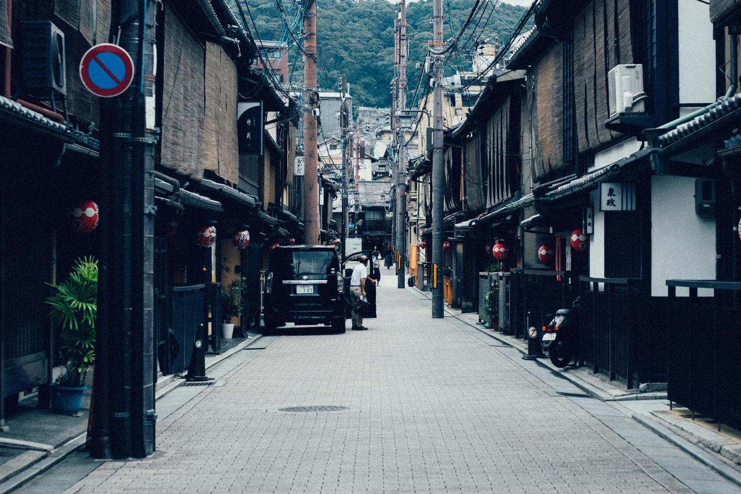 A quiet stone-paved street of wooden houses in Gion, with the hills of Higashiyama behind