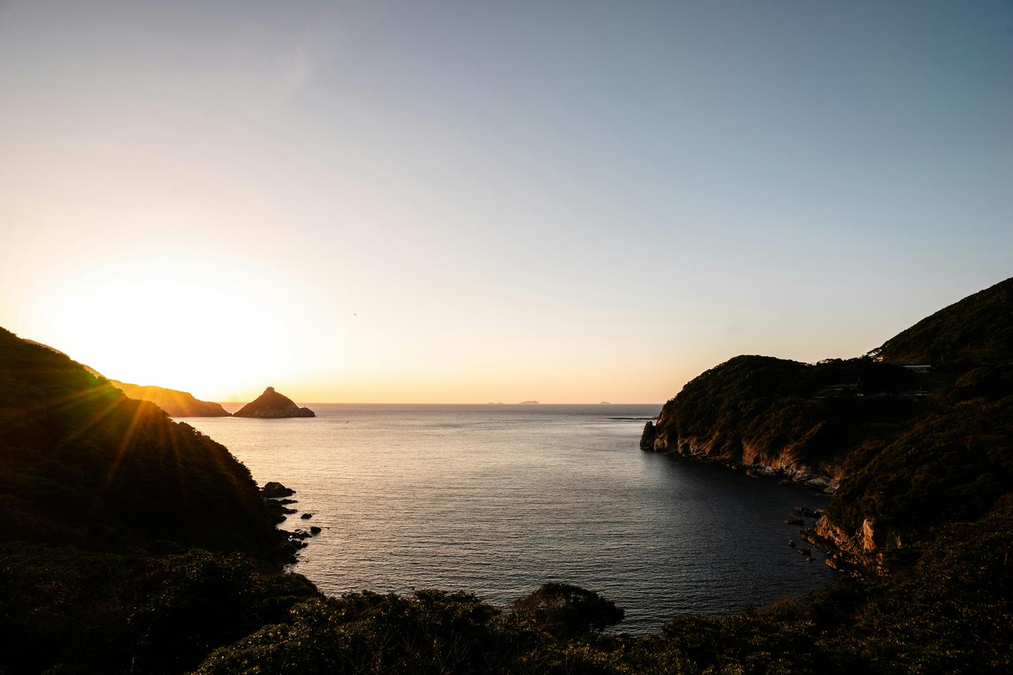 The sun sets over a quiet bay between green headlands on the Goto Islands.