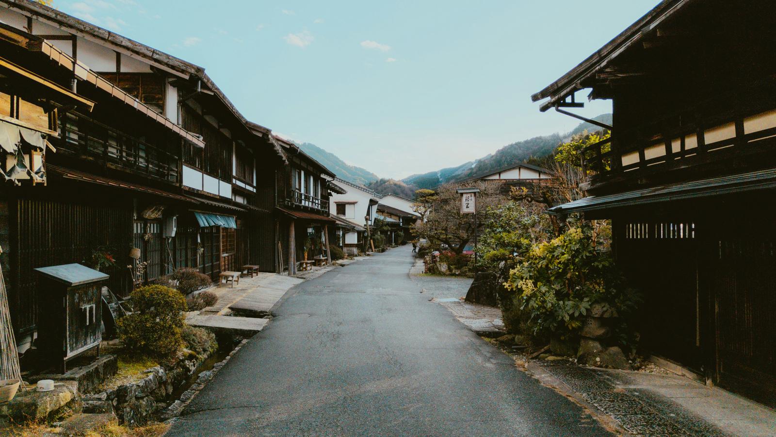The quiet main street of Tsumago, lined with dark wooden inns, with mountains behind