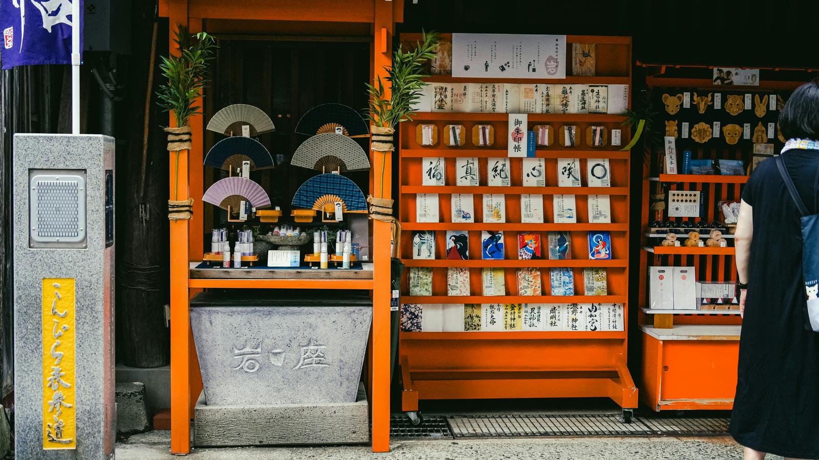 A visitor looks at omamori charms laid out at an orange wooden shrine counter