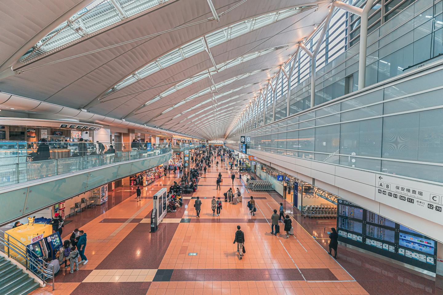 Travellers walking through the long, light-filled hall of a Haneda Airport terminal