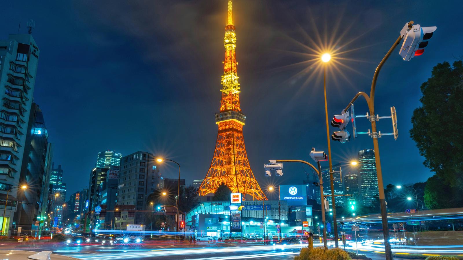 Tokyo Tower lit orange at night above a street with trails of car lights