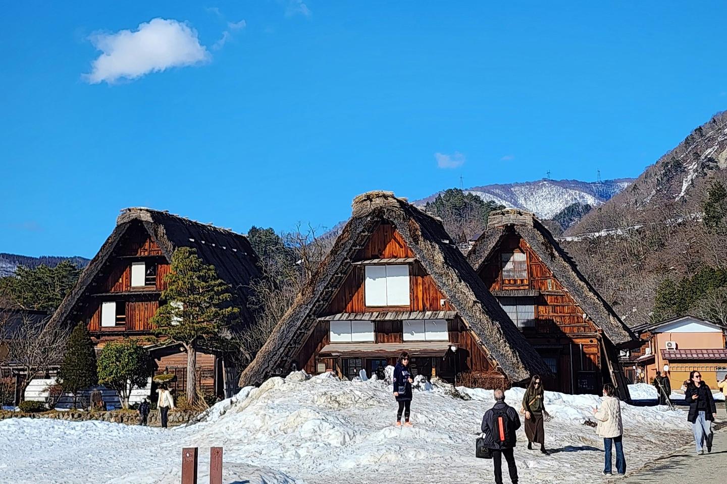 Visitors walking past three thatched farmhouses on a bright winter day in Shirakawa-go