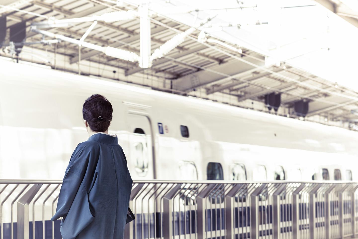 A traveller in a grey jacket waiting alone on a Shinkansen platform at Kyoto Station