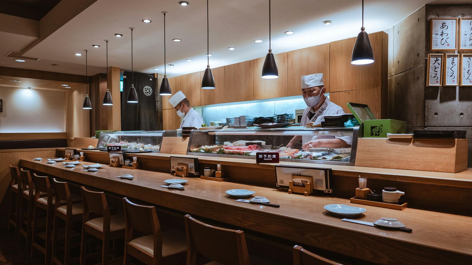 A long wooden sushi counter in Ginza with chefs at work behind it and the seats still empty