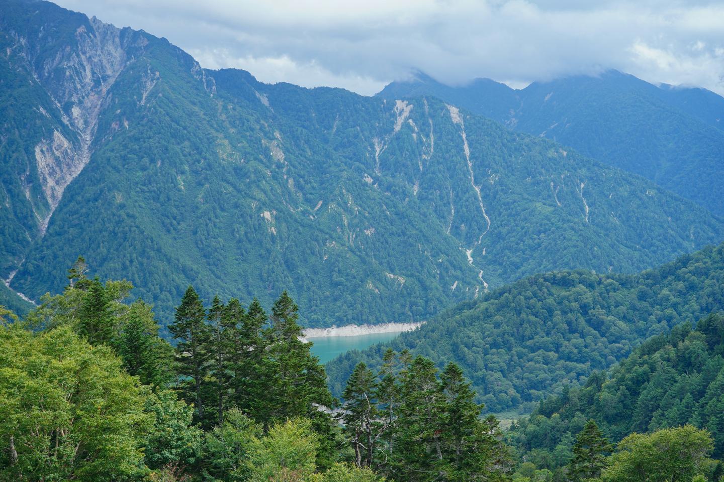 Turquoise Lake Kurobe lies deep in a forested valley between steep mountain ridges.