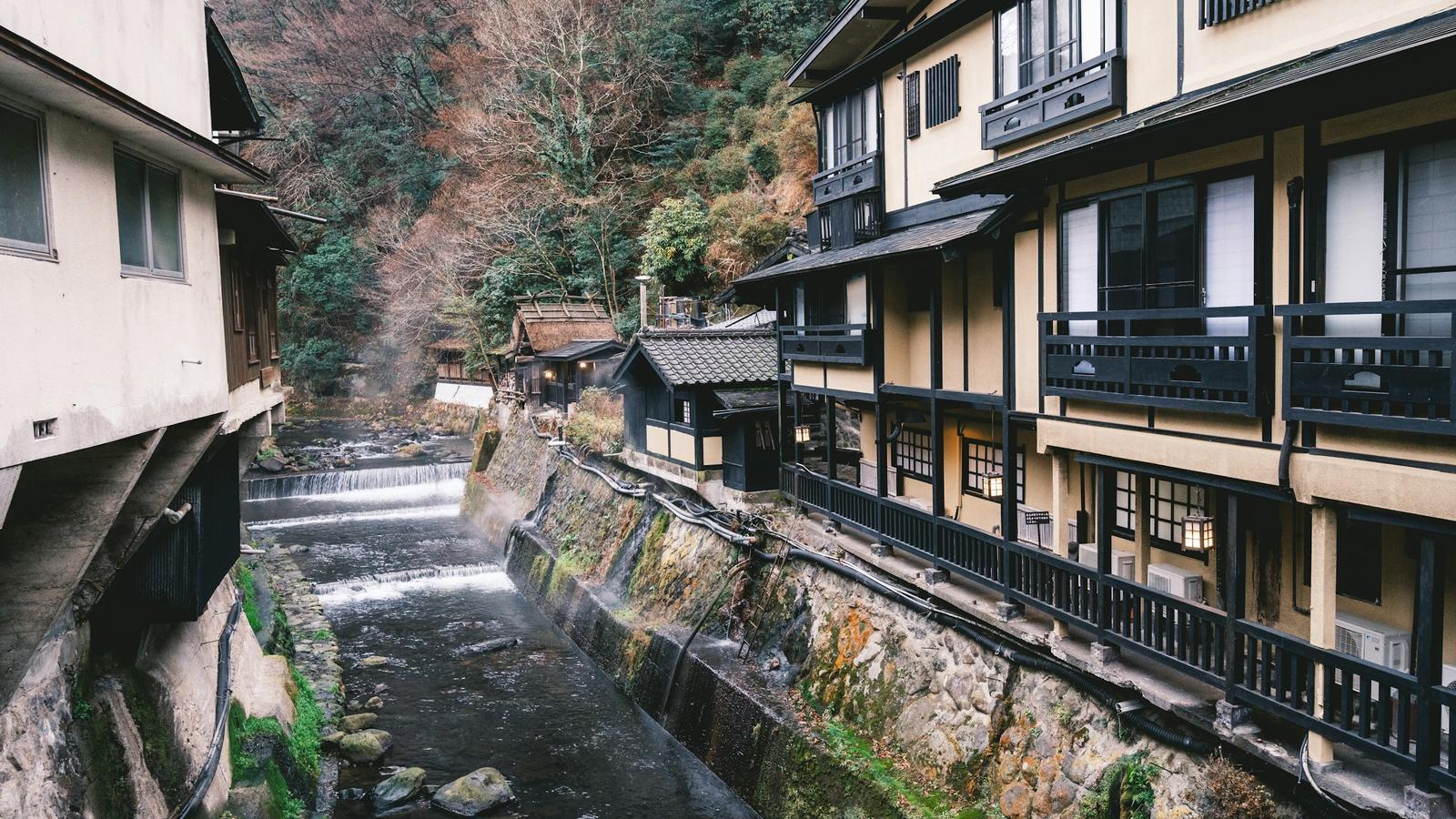 Wooden inns with long balconies along a narrow river in a forested hot spring village