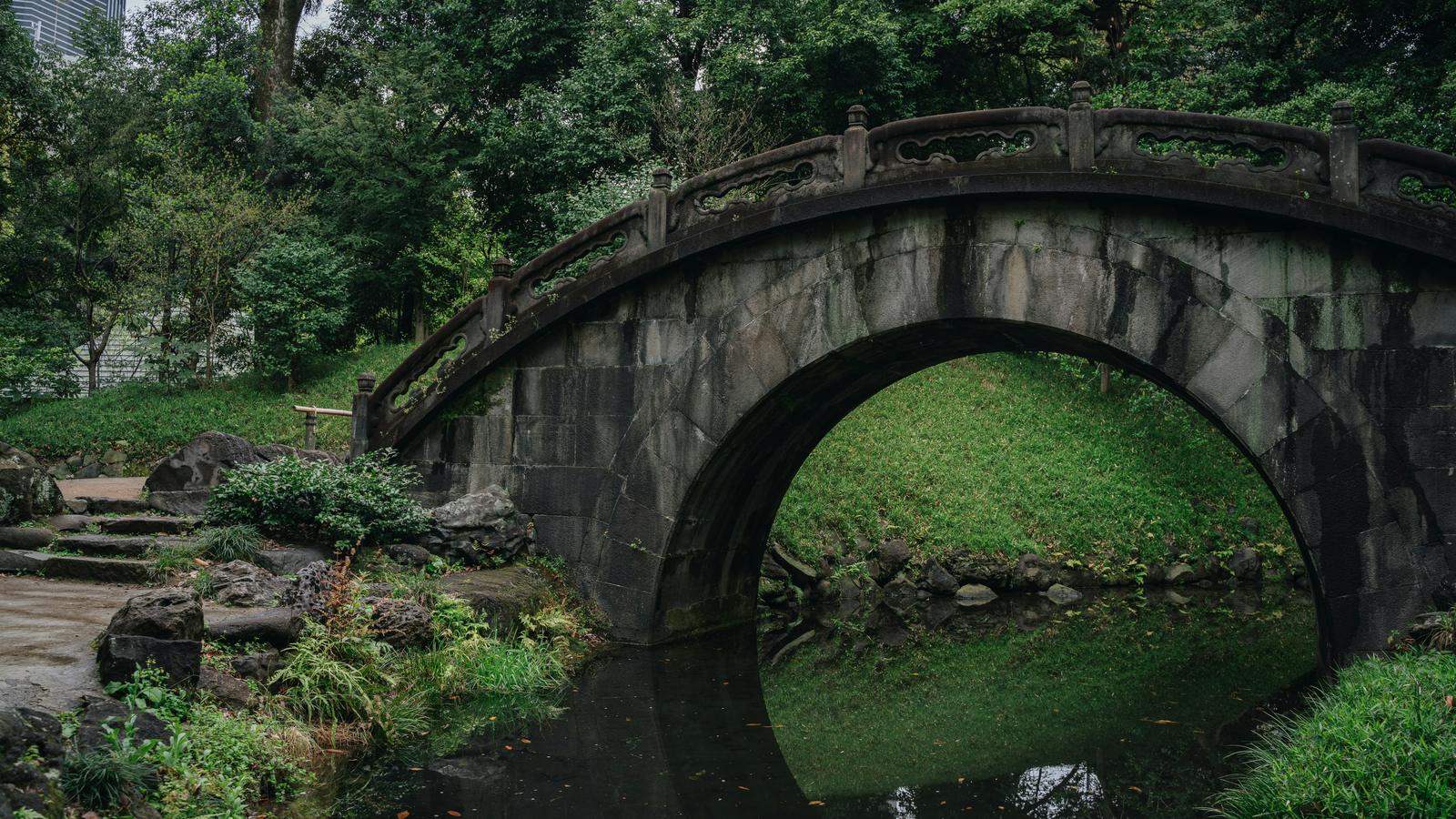 A stone arch bridge over a pond among green trees at Koishikawa Korakuen in Tokyo