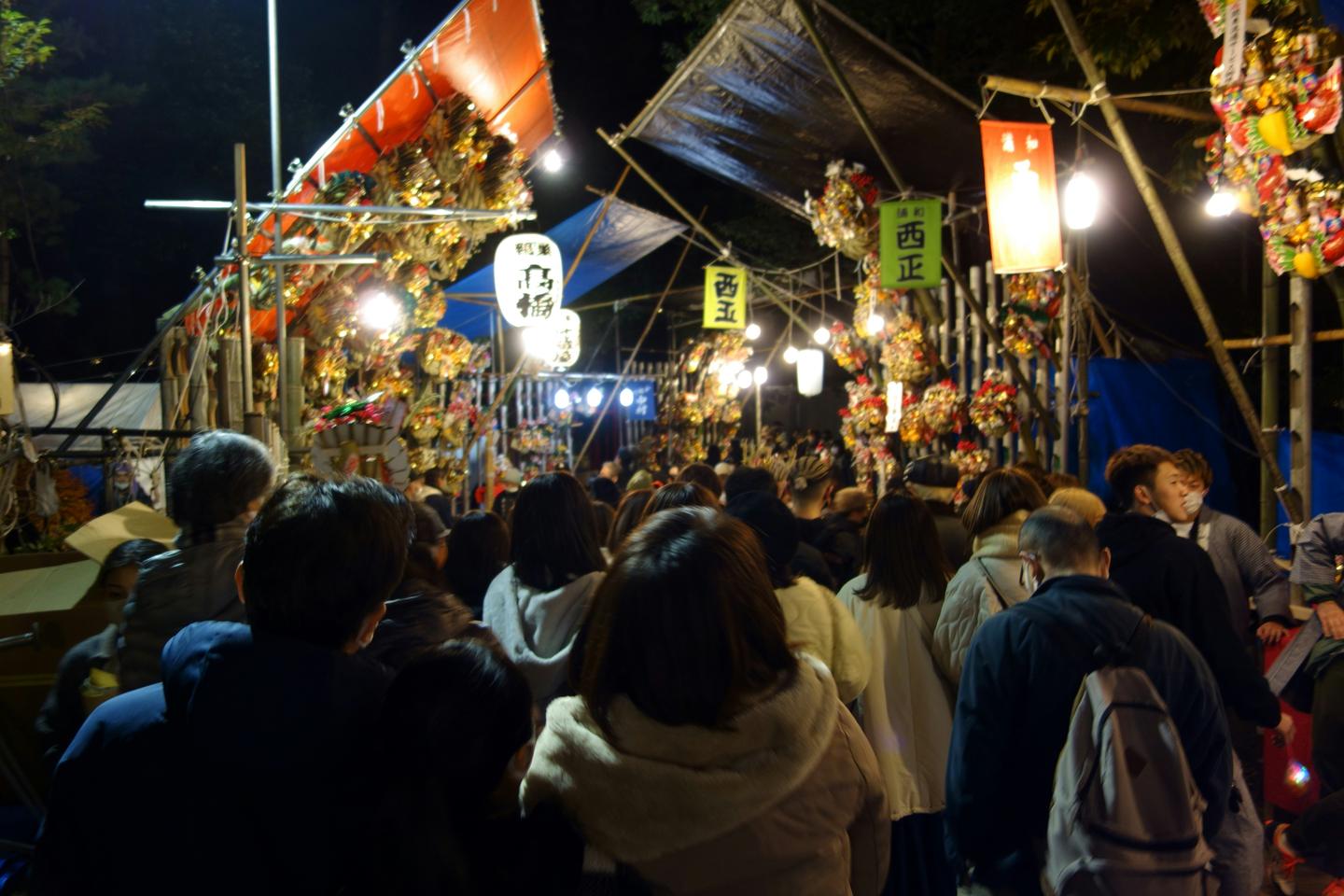 A dense evening crowd moving between lantern-lit kumade stalls at a tori no ichi fair