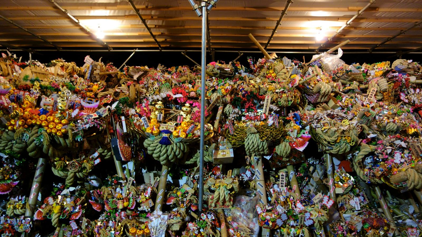 Decorated kumade rakes with straw rope and lucky ornaments stacked under a stall roof at night