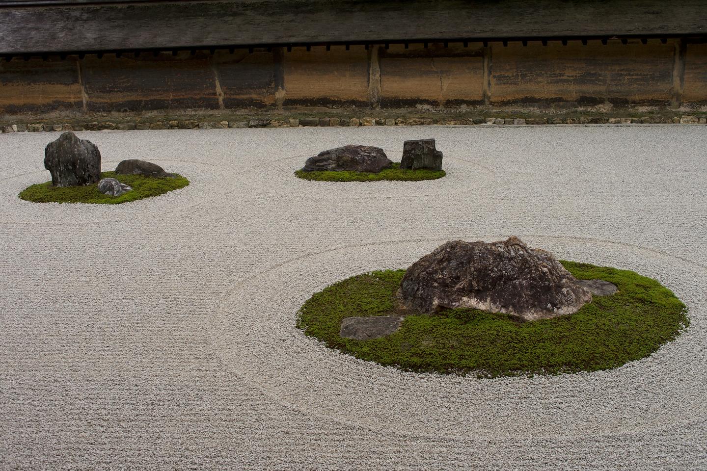 Three mossy islands with dark rocks in a raked white gravel garden