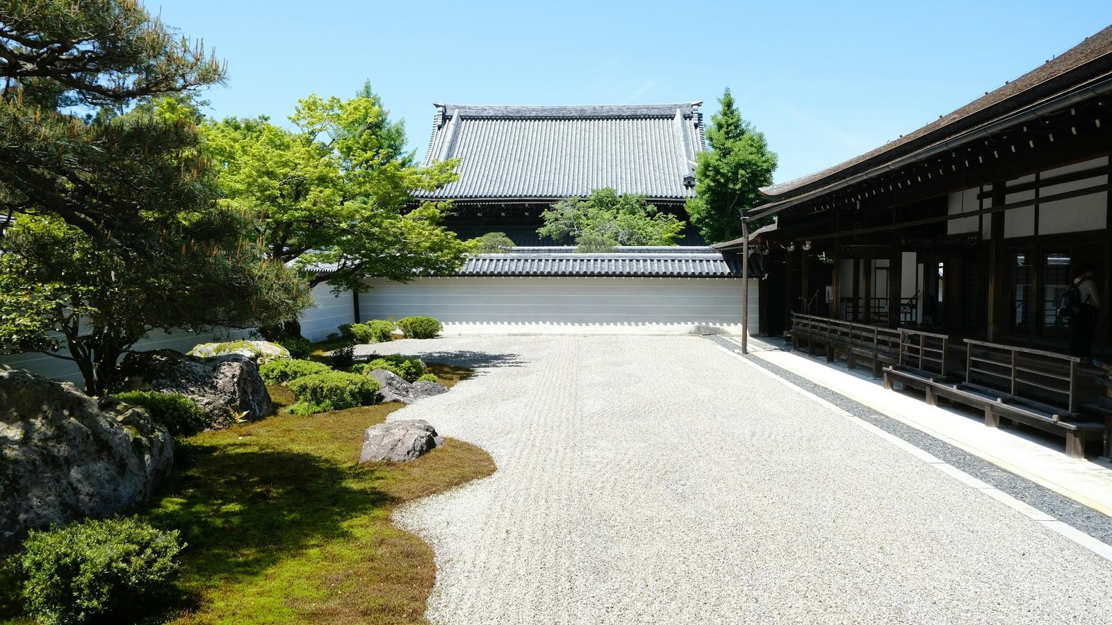 A raked gravel garden with moss and pine trees in front of a temple hall on a clear morning
