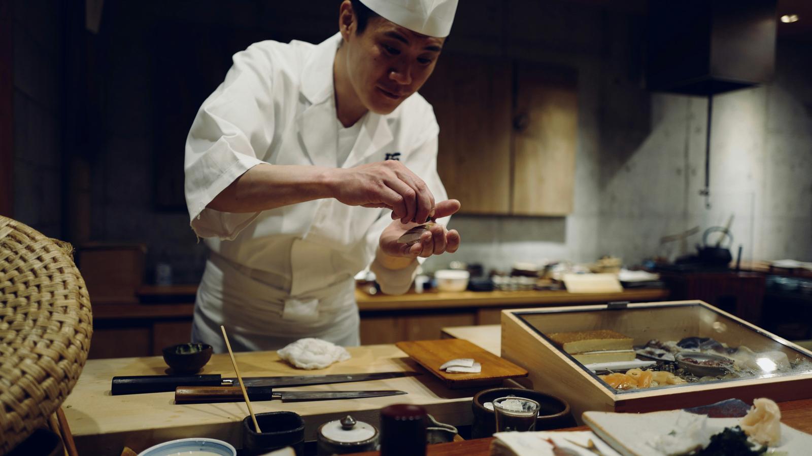 Un cocinero de blanco formando sushi en una barra de madera