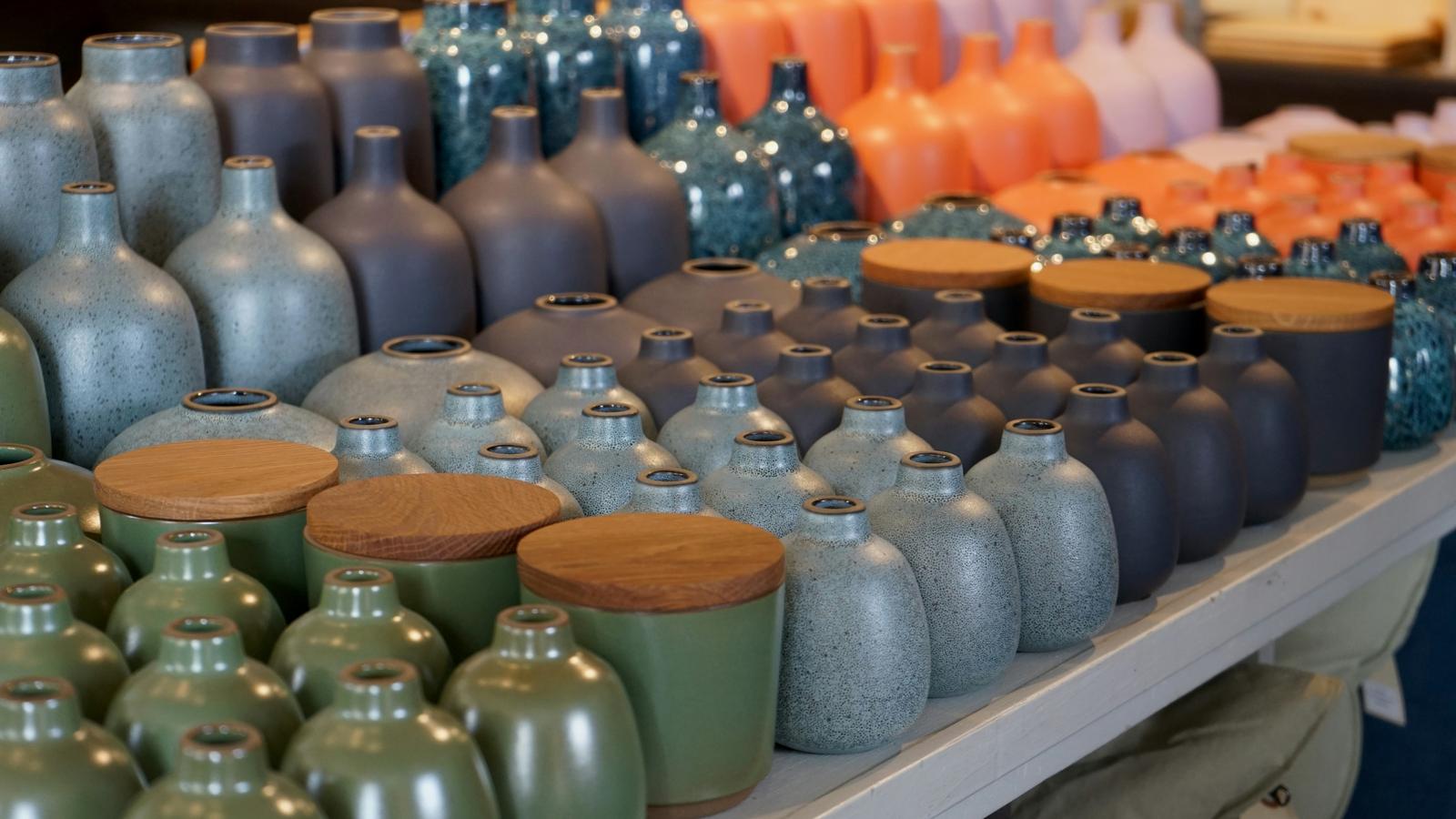 Hileras de tarros y jarrones de cerámica esmaltada con tapa de madera sobre una mesa de tienda