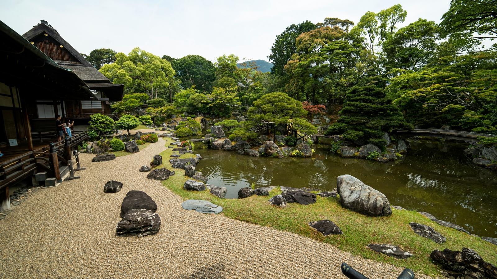 Un jardín japonés con grava rastrillada, rocas y un estanque junto a una casa de madera