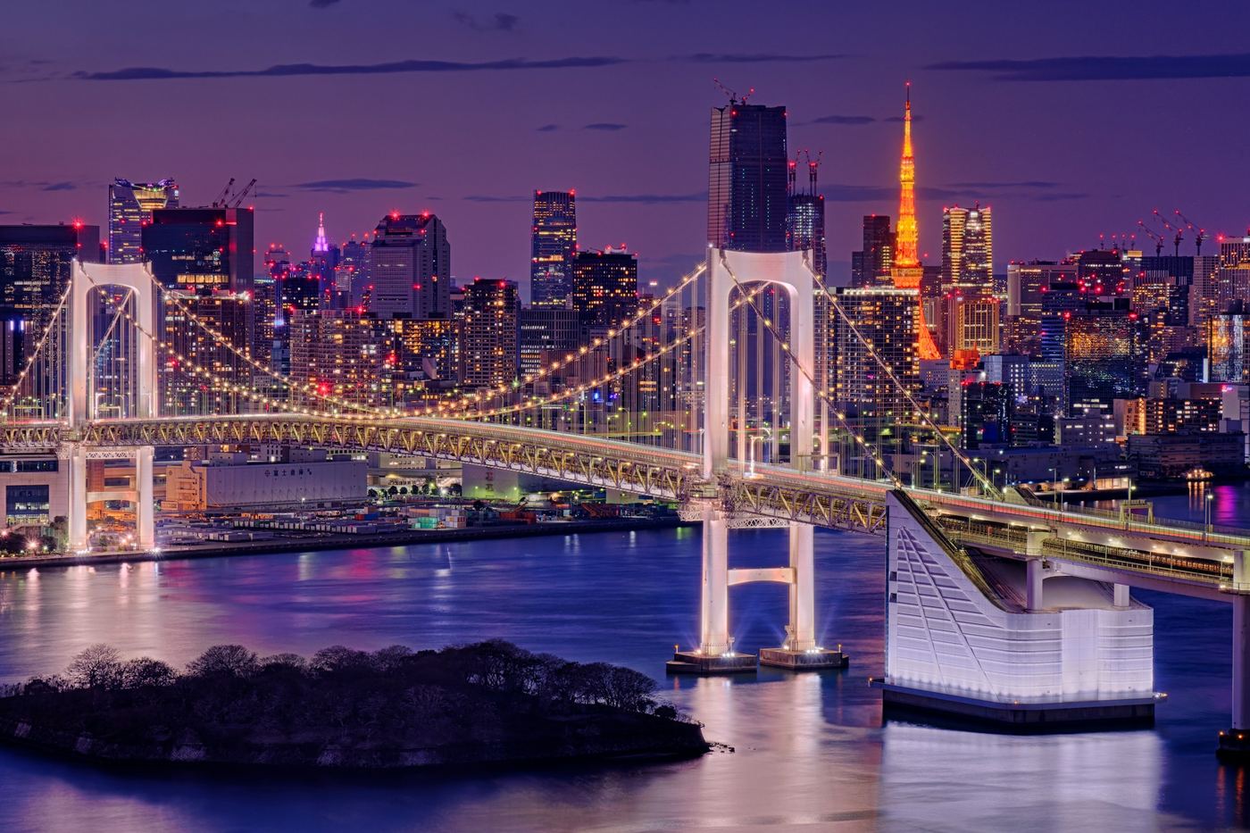 Rainbow Bridge and the Tokyo skyline lit at dusk, with Tokyo Tower behind