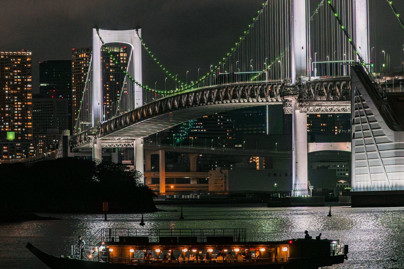 A lit boat on Tokyo Bay at night below Rainbow Bridge