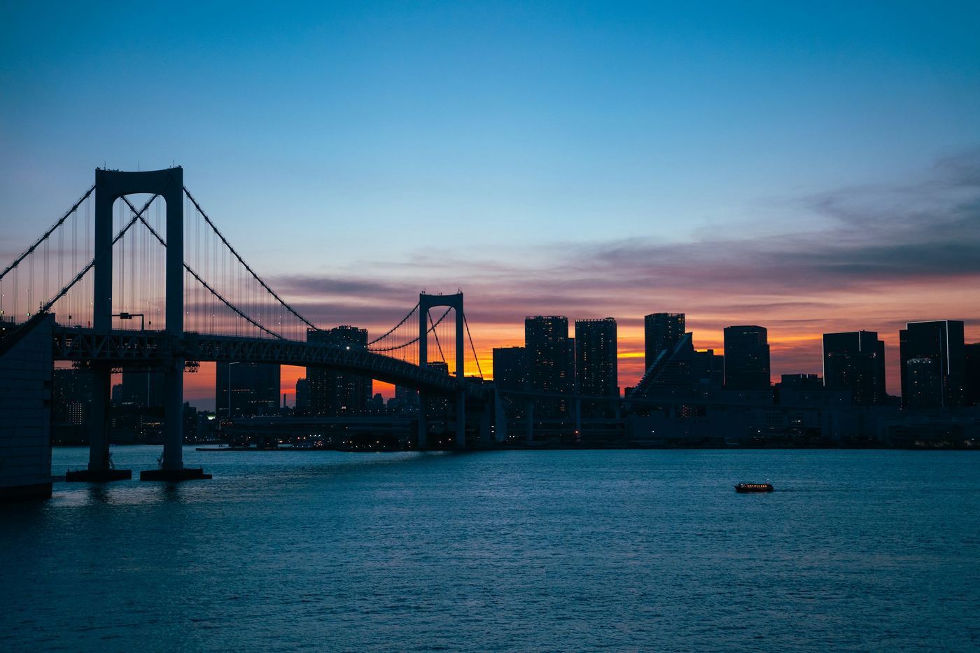 Rainbow Bridge in silhouette against an orange sunset over Tokyo Bay