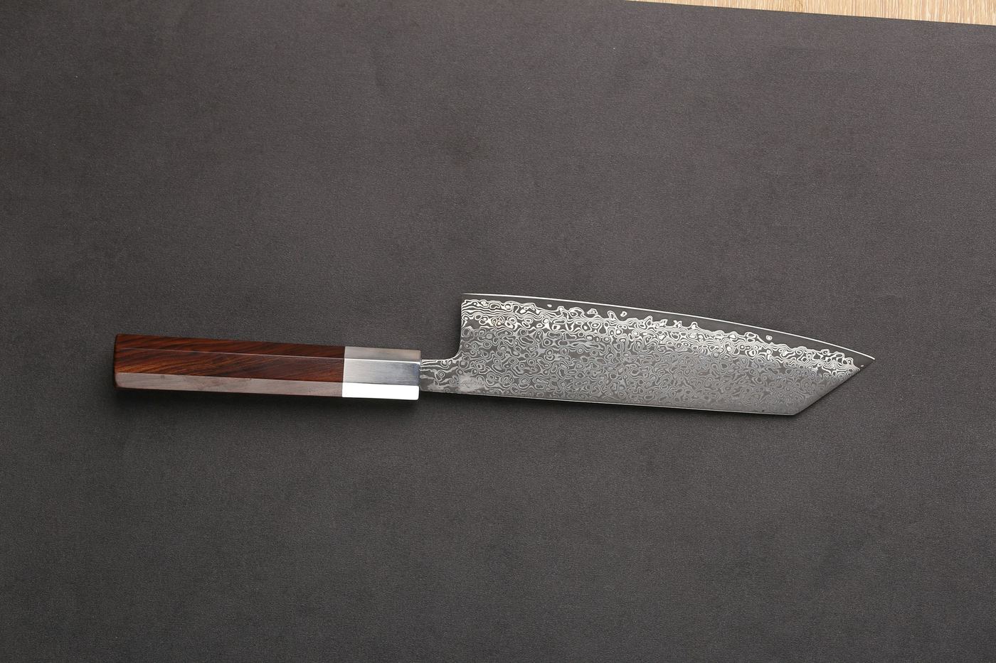 A knife with a patterned blade and wooden handle on a grey surface