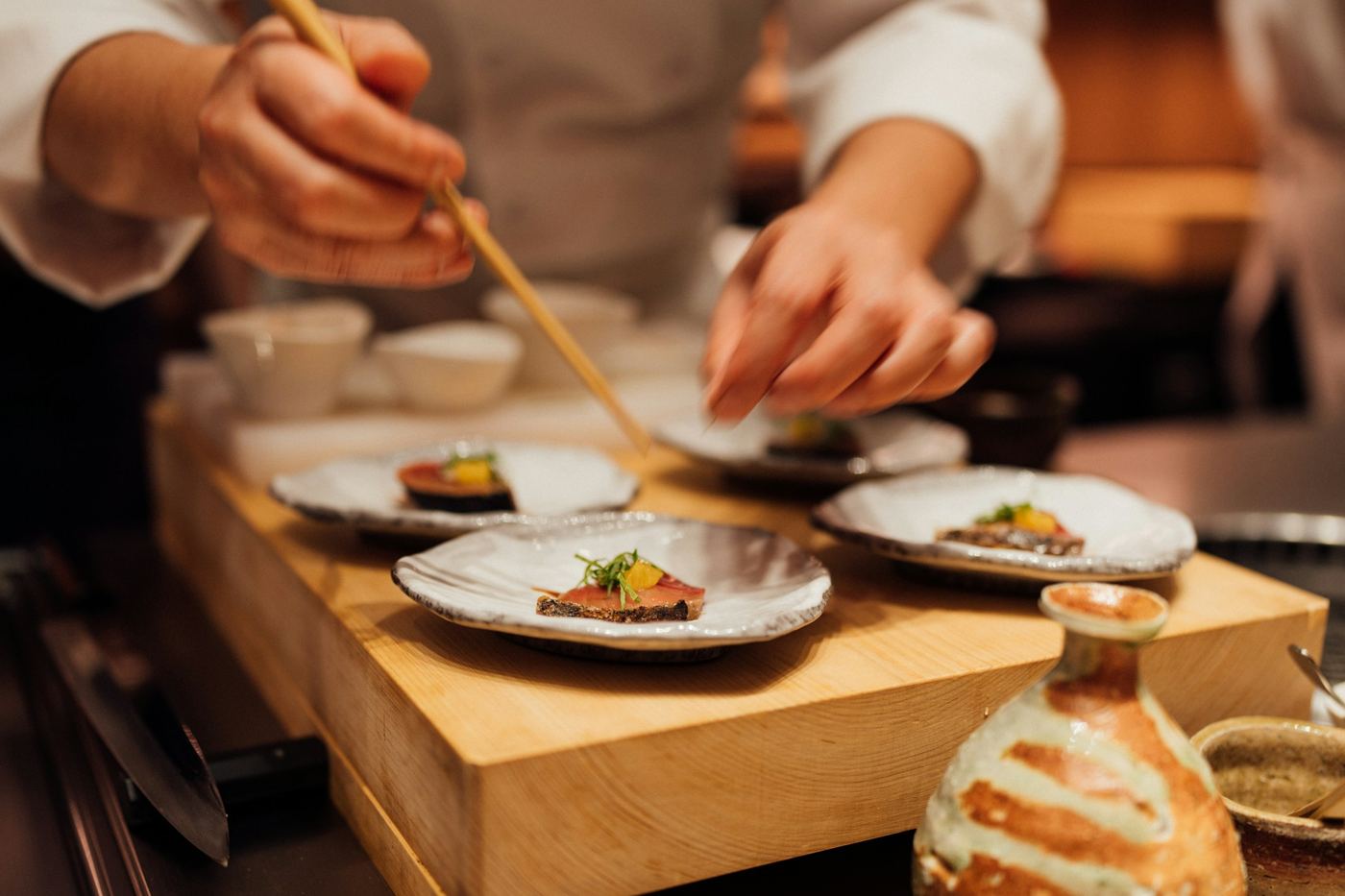 A chef's hands placing food on small plates at a wooden counter